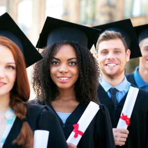 Photo d'un groupe d'étudiant debout l'un derrière l'autre, chacun habillé d'une toge et tenant un diplôme.